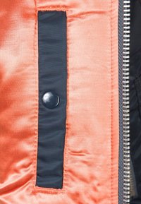 Gros plan sur la doublure d'une veste orange avec une patte à bouton-pression noir et une fermeture éclair argentée le long du bord.