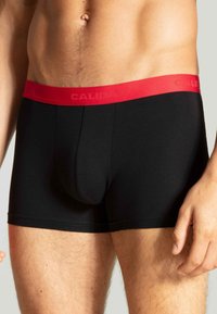 Zwarte boxershorts met een rode elastische tailleband met de tekst "CALIDA." De stof lijkt zacht met een taillerende pasvorm en minimale naden.