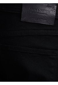 Černé džíny z denimu s koženou nášivkou s vyraženým textem, viditelnými švy a hladkým povrchem. Design zadní kapsy je jednoduchý a funkční.