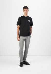 Camiseta negra de manga corta con un gráfico en el pecho, combinada con pantalones de chándal ajustados de color gris claro y zapatos negros.