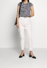 Marinblus med vitt abstrakt mönster, vita högmidjade byxor och svarta slingback-klackar med kraftiga klackar och strukturerad yta.