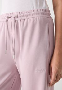 Light pink sweatpants made of soft fabric, featuring an elastic waistband with drawstring and a small embroidered logo on the side.