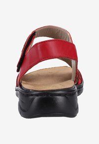 Sandal en cuir rouge avec des brides croisées et une semelle en caoutchouc noir. Dispose d'un coussin de pied et d'une sangle réglable pour le confort. Texture lisse.