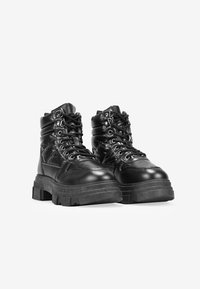 Botas de tobillo de imitación cuero negro con suela gruesa, cordones en la parte frontal, cuello acolchado y detalles de costura. Acabado texturizado con ojetes metálicos.