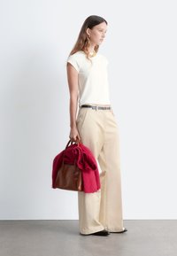 Cremefarbenes Kurzarm-Oberteil, beige weite Hose, schwarzer Gürtel und braune Handtasche mit einem roten Schal, der darüber drapiert ist. Glatte Texturen überall.