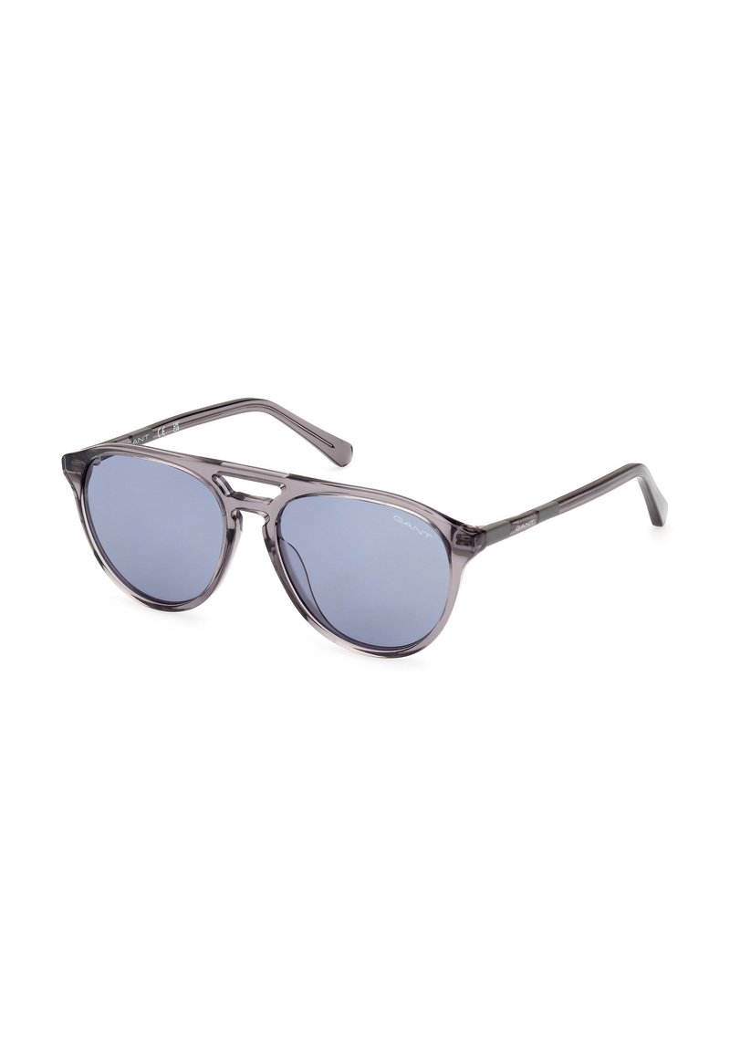 Gafas de sol grises con lentes ahumados azules, montura transparente ligera y forma aerodinámica. Presentan un sutil logotipo en la patilla.