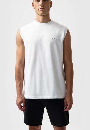 T-shirt sans manches blanche en tissu léger, comportant un petit logo brodé sur la poitrine, assortie à un short noir.