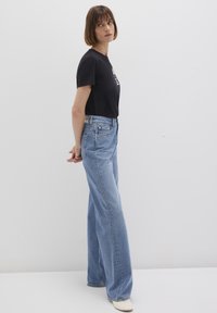 Black short-sleeve t-shirt with graphic print, paired with high-waisted light blue wide-leg jeans. White shoes complete the look.