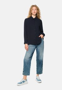 Navy long-sleeve button-up shirt with a collar, paired with loose faded blue jeans and light blue accents on the sneakers.