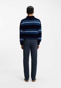 Marineblauer Pullover mit blauen und hellblauen Streifen; kombiniert mit dunkelgrauer Hose und dunklen Schuhen; glatte Textur, lockere Passform.