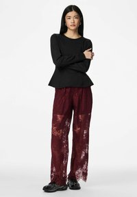 Melns garām piedurknēm tops ar pepluma malu, kombinēts ar caurspīdīgām bordo mežģīņu plats kāju biksēm un melniem sporta apaviem.