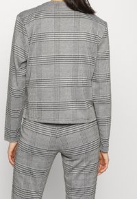Ensemble blazer et pantalon à carreaux gris et noirs, présentant une coupe structurée, des manches longues et un tissu texturé avec un motif géométrique.