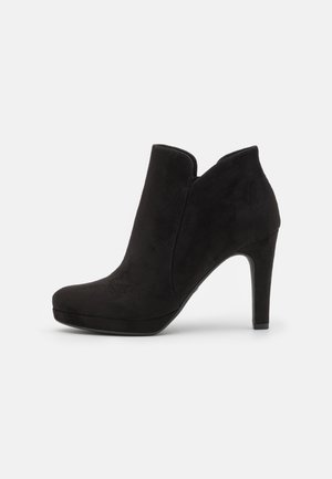 Bottine pour femme en daim noir avec bout arrondi, semelle compensée et talon haut effilé, présentée sur un fond blanc.