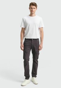 Grijze cargobroek met meerdere zijzakken, gecombineerd met een effen wit T-shirt en witte sneakers. Eenvoudig, casual ontwerp.