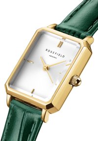 Reloj rectangular dorado con una esfera blanca texturada, agujas doradas y una correa de cuero verde con un acabado suave y acentos cosidos.