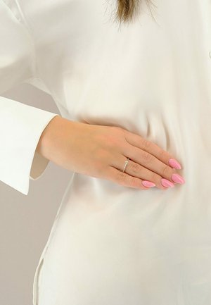 Anello d'argento su una mano con unghie lunghe, rosa, a forma di mandorla, appoggiata su una blusa bianca liscia con ampie maniche, caratterizzata da una morbida texture del tessuto.