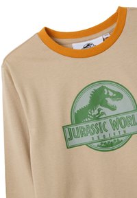 Beige lange mouw shirt met een groen Jurassic World Rebirth-logo en een oranje geribbelde kraag. Zacht materiaal met een gladde textuur.