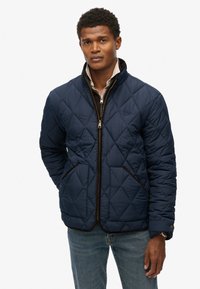Navy gewatteerde jas met een staande kraag, voorzien van een ritsluiting, zijzakken en bruine afwerking langs de randen.