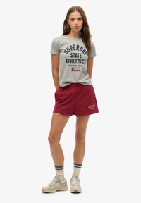 Grå kortærmet T-shirt med navy print, bordeaux shorts, beige sneakers og creme strømper med navy striber, med en afslappet pasform.