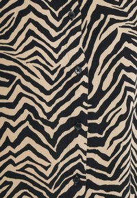 Tissu beige avec des rayures zèbre noires et une rangée de quatre boutons noirs au centre.