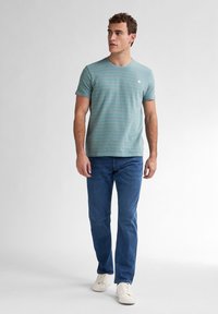 T-shirt à manches courtes rayé bleu avec un col rond, associé à un jean bleu foncé et des baskets blanches. Design épuré avec un style décontracté.