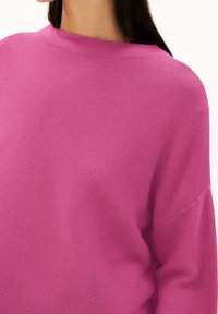 Pull surdimensionné en rose vif, fabriqué en tissu tricoté texturé. Présente une encolure large et une coupe décontractée, avec des coutures d'épaule tombantes.