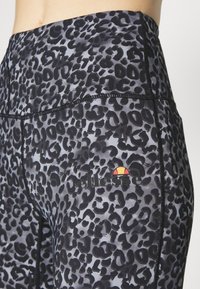 Legginsy o wysokim stanie w czarno-szarym wzorze w panterkę. Posiadają płaskie szwy oraz małe logo w czerwonym i żółtym kolorze na lewym udzie.