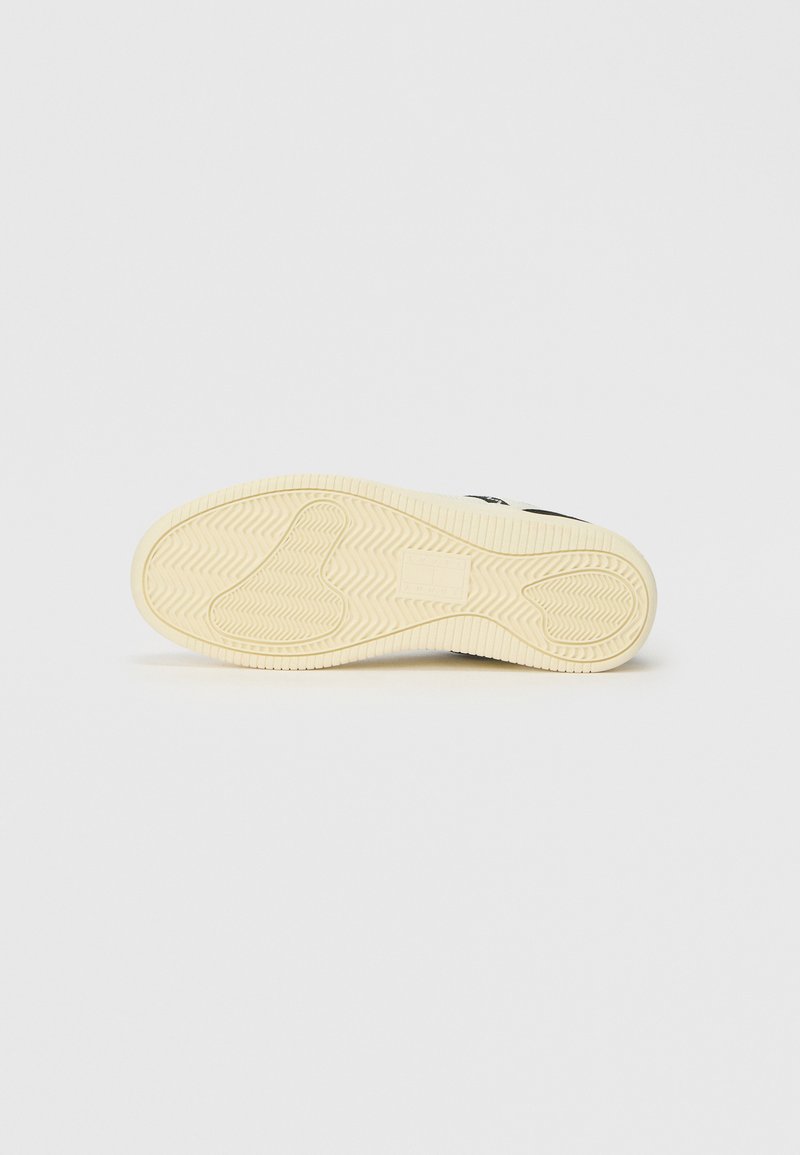 Sneaker sole in cream rubber, textured with zigzag patterns and a smooth section, designed for traction, featuring a minimalist design.