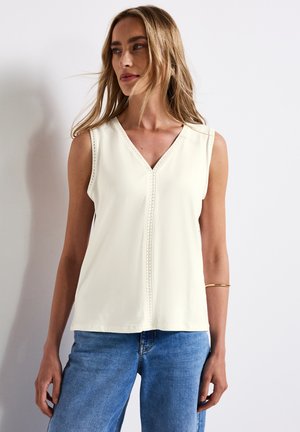 Top senza maniche, con scollatura a V in tessuto avorio dalla superficie liscia, con cuciture decorative lungo il colletto. Abbinato a jeans in denim.