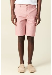 Vaaleanpunaiset farkut, jotka on valmistettu puuvillasekoitteesta, joissa on nappikiinnitys, sivutaskut ja suora leikkaus, yhdistettynä vaaleanbeigeihin liukukenkään.