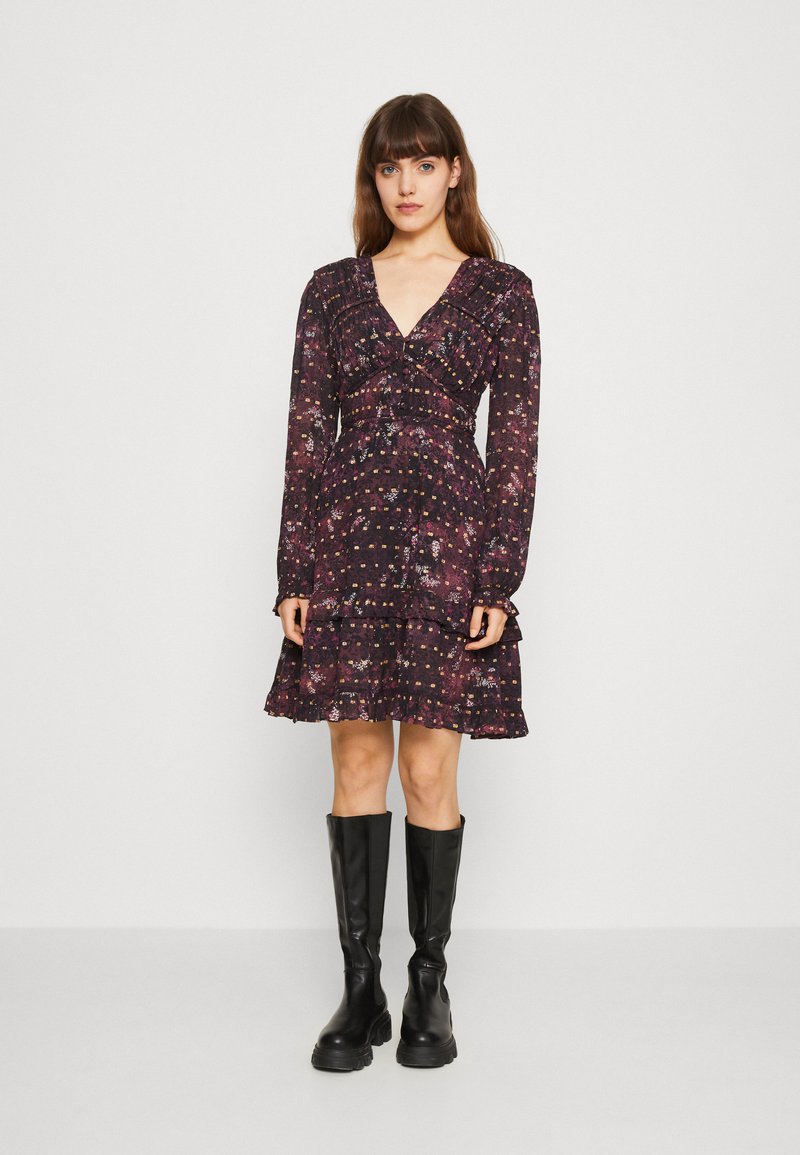 Vestido preto floral com um decote em V profundo, mangas longas e uma bainha com babados. O tecido é leve e apresenta um padrão texturado. Combinado com botas altas pretas até ao joelho.