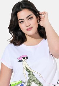 Maglietta bianca a maniche corte con una grafica colorata di una figura di moda con un cerchietto rosa e un outfit con stampa leopardata, mentre tiene delle borse da shopping.