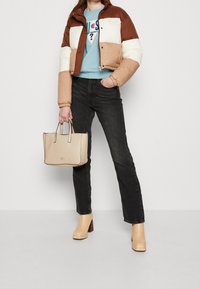 Kurtka puchowa w kolorze brązowym, kremowym i beżowym, w połączeniu z jasnoniebieską koszulą, czarnymi dżinsami, beżową torebką i masywnymi beżowymi szpilkami.