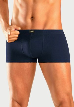 Muscular male torso and upper legs wearing dark blue fitted boxer briefs, pulling waistband outward, plain light background.