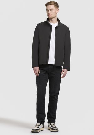 Sort jakke med lynlås foran og høj krave, kombineret med en hvid t-shirt, sorte jeans og sort-hvide sneakers.