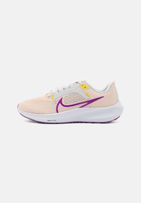 Zapatilla de running ligera de malla en color melocotón con acentos en púrpura, que cuenta con una media suela blanca, superficie texturizada y un logotipo prominente en el lateral.