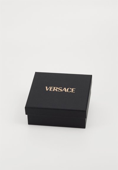 Musta suorakulmainen laatikko, joka on valmistettu teksturoidusta materiaalista ja jossa on saranoitu kansi. Ylhäällä on kultainen "VERSACE"-logo.