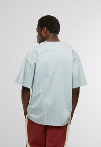 Gaiši zils īsām piedurknēm krekls ar dzeltenām vertikālām svītrām, brīva piegriezuma, apaļš kakla izgriezums un mīksta kokvilnas faktūra.