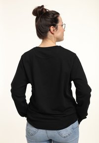 Sudadera negra, cuello redondo, mangas largas, textura suave, puños y dobladillo elásticos, vista desde la parte de atrás, combinada con jeans azul claro.