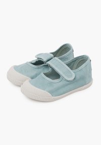 Zapatillas de lona azul claro con una correa de velcro, punta redondeada y suelas de goma blanca. Capas de punta texturizadas y detalles de costura en los laterales.