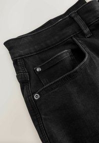 Black denim jeans with a front pocket, visible stitching details, and metal hardware. Fabric appears textured with a subtle sheen.