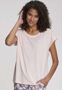 Hele roosa lühikeste varrukatega särk, mis on valmistatud pehmest kangast, lõdva lõikega ning millel on ees valge tekst "Uni lahendab kõik probleemid."