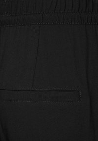 Nahaufnahme eines schwarzen Stoffs mit elastischem Bund und horizontaler Leistentasche am Kleidungsstück.