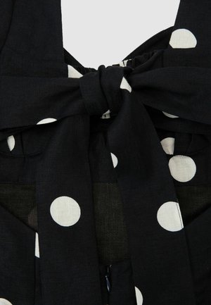 Material negru cu buline albe mari, legat într-o fundă peste o închidere ascunsă cu fermoar.