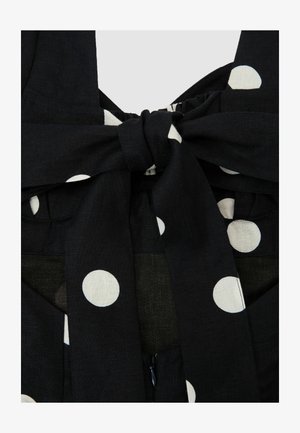 Czarna tkanina z dużymi białymi kropkami, zawiązana w kokardę na ukrytym zamku błyskawicznym.