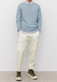 Maglione azzurro chiaro sopra una camicia grigia con colletto, abbinato a pantaloni cargo crema con tasche laterali e stivali verde oliva con lacci.