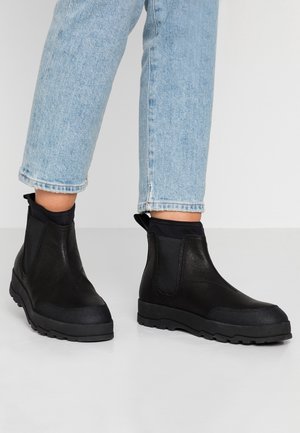 Bottines noires avec une tige en cuir lisse, des panneaux latéraux élastiques et des semelles en caoutchouc. Elles sont dotées d'une languette à l'arrière pour un enfilage facile.