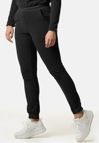 Schwarze Jogginghosen aus einem weichen, dehnbaren Stoff, mit schmal zulaufenden Beinen, elastischem Bund und Seitentaschen, kombiniert mit weißen Sneakers.