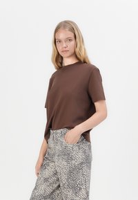 Brun kortermet T-skjorte med rund hals, sammen med lyse bukser med leopardmønster. Stoffet ser glatt og uformelt ut.