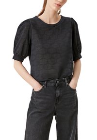 Sort kortærmet bluse med pufærmer, der har et struktureret mønster og rund halsudskæring, parret med høj talje sorte jeans.